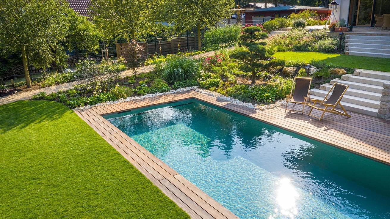 Living pool from above with green lawn, clear blue water on wooden terrace